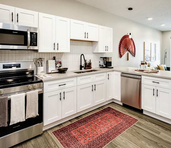 A kitchen with white cabinets and a red rug on the floor.