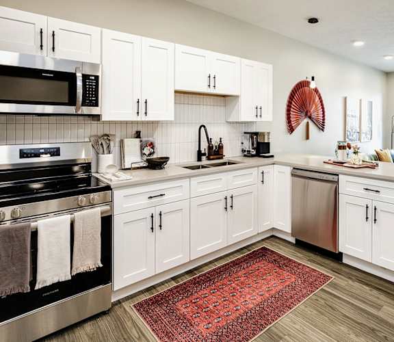 A kitchen with white cabinets and a red rug on the floor.