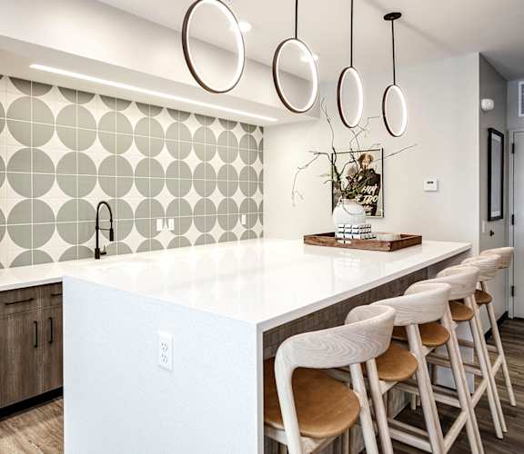 A kitchen with a white counter top and wooden chairs.