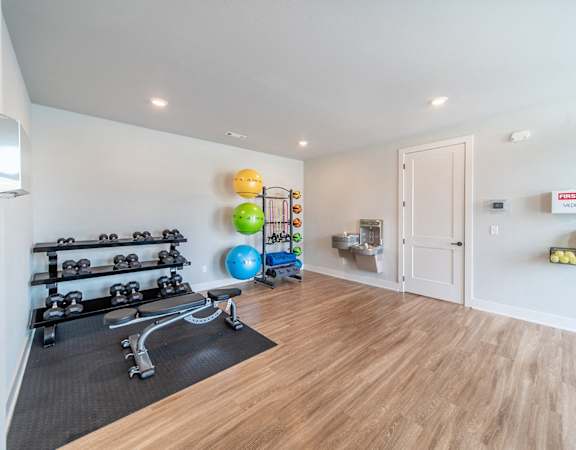 A room with a wooden floor and a wall-mounted rack of dumbbells.