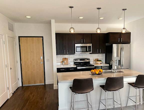 A kitchen with a white counter top and brown chairs.
