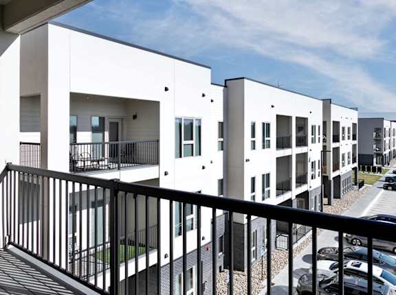 A row of white townhouses with black railings and cars parked in the driveway.