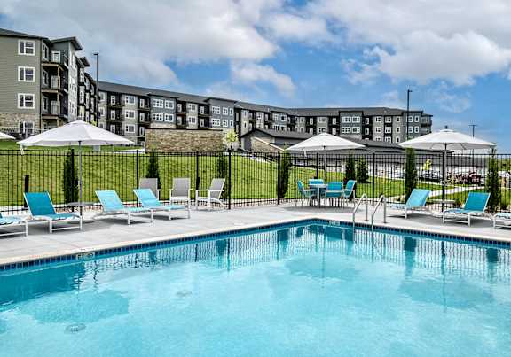 a swimming pool with blue chaise lounge chairs and umbrellas in front of an apartment