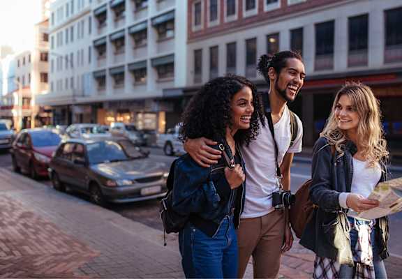 Three friends are walking down a street, looking at a map.