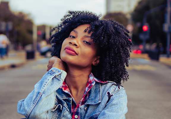 A woman with curly hair wearing a denim jacket is posing for a picture.
