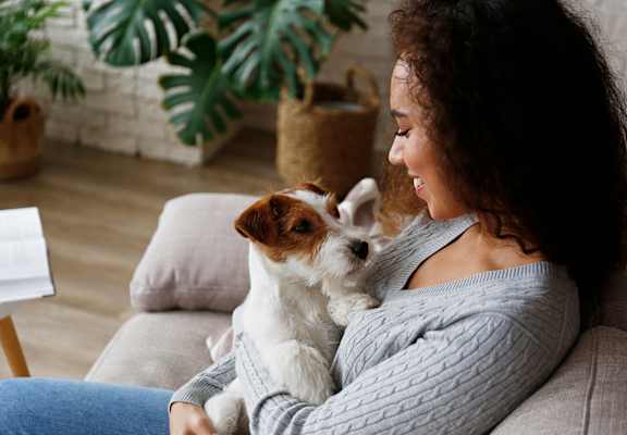 A woman is sitting on a couch holding a small dog.