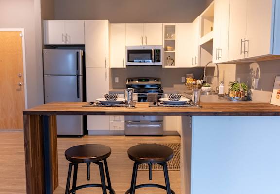 A kitchen with a refrigerator, microwave, and a counter with two stools.