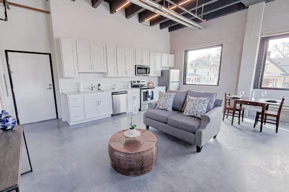 A modern kitchen with white cabinets and a grey couch.