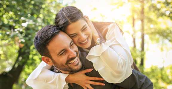 A man is carrying a woman on his back in a park.