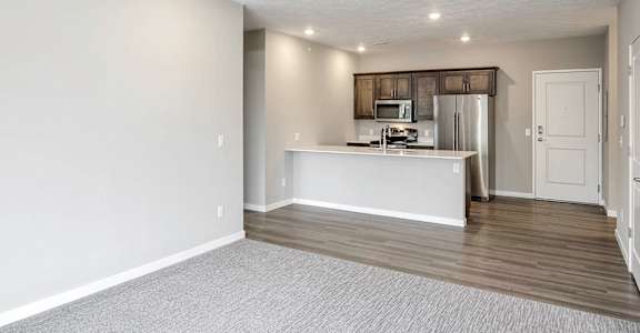 an empty living room with a kitchen in the background