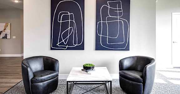 two chairs and a table in a living room with paintings on the wall