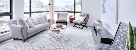 A living room with a grey couch, a chair, a table, and a large window with a view of the city.