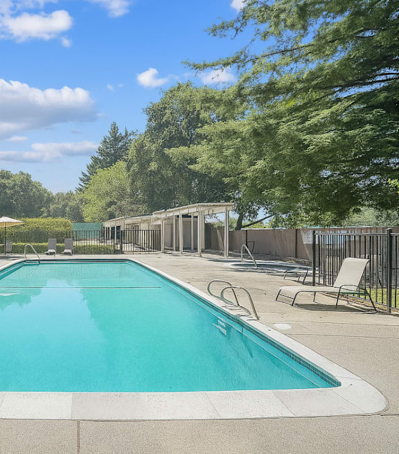 A large outdoor swimming pool surrounded by trees and a fence.