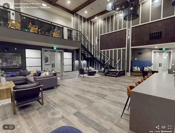 A modern interior of a clubroom with a staircase, seating area, and a bar.