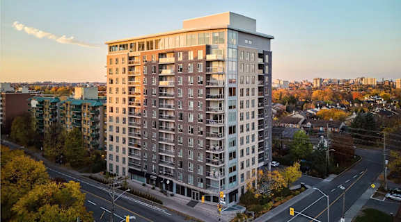 A large apartment building is situated on a street corner with a road in front of it.