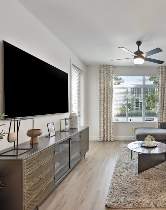 A living room with a grey couch, a black television, and a ceiling fan.
