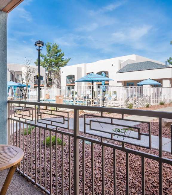 A balcony with a table and a chair overlooking a pool area.