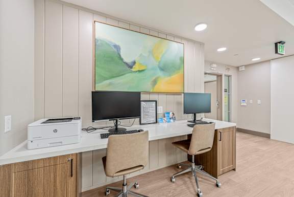 A room with a desk, chairs, and a painting on the wall.
