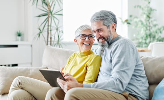 a man and woman sitting on a couch looking at a tablet