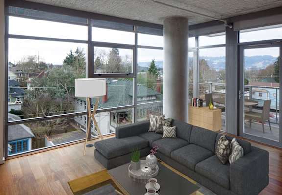 A grey couch with pillows sits in a room with a view of the outdoors.