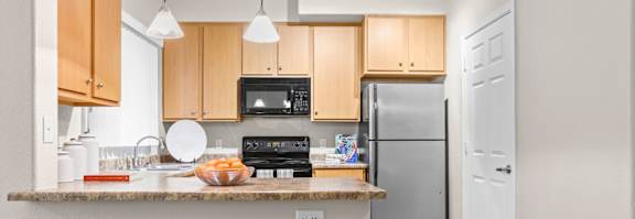 A kitchen with a refrigerator, microwave, and bar stools.