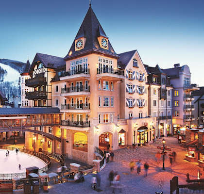 A large building with a clock tower and an ice rink in front.