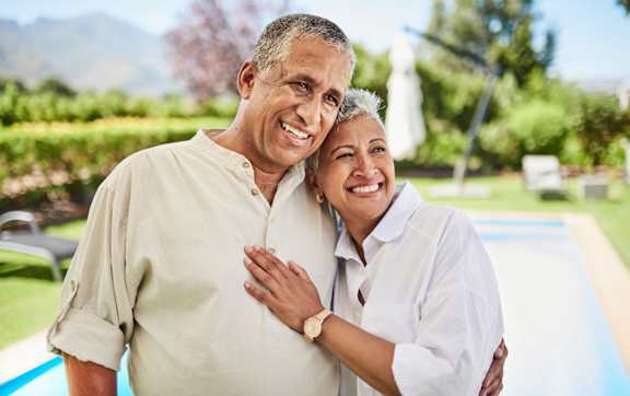 An older couple is standing close together, smiling and embracing.