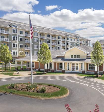 A large building with a flag on top and a circular driveway in front at Axis at Lakeshore Apartments, MA,02324