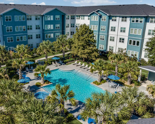 A large swimming pool surrounded by palm trees and lounge chairs in front of a multi-story building.