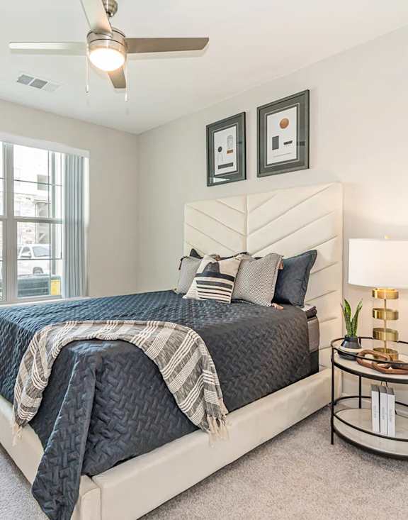 A bedroom with a bed, a plant, and a ceiling fan.