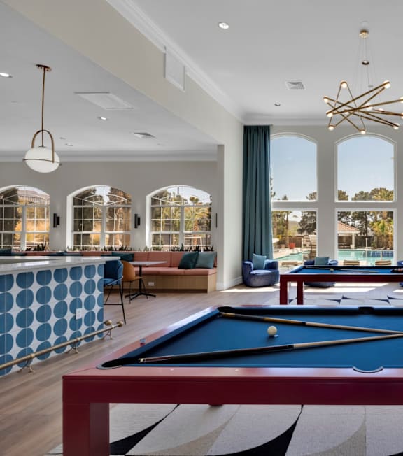 a game room with a pool table and a view of a bar and windows