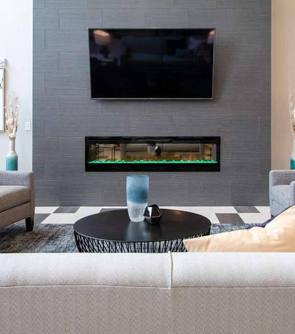 A living room with a grey couch, a black coffee table, a flat screen TV, and two paintings on the wall at Avonlea in Lakeville, MN