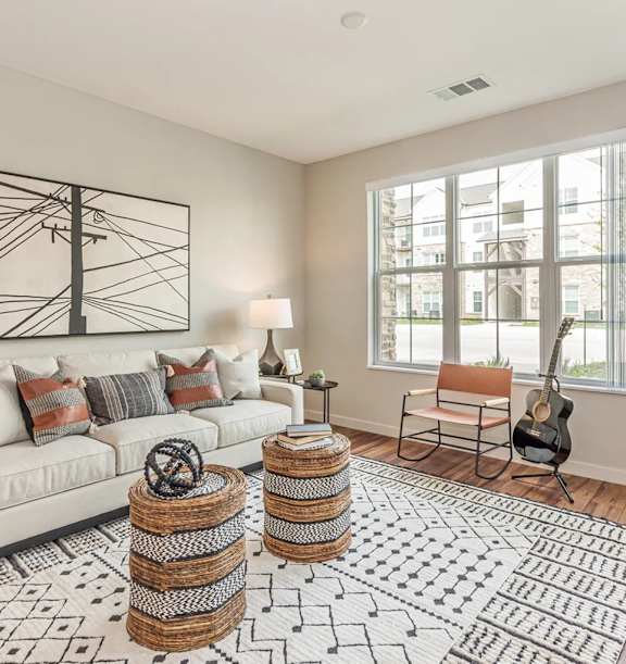 A living room with a white couch, a guitar, and a large window.