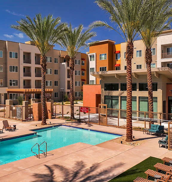 A pool surrounded by palm trees and chairs in front of apartment buildings.