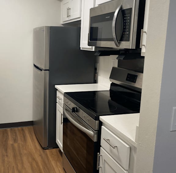 A black refrigerator and microwave in a kitchen with white cabinets.