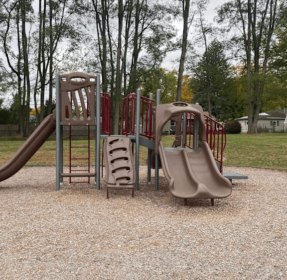 A playground with a red and grey slide and a brown slide.
