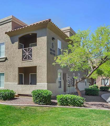 an apartment building with a green lawn and trees
