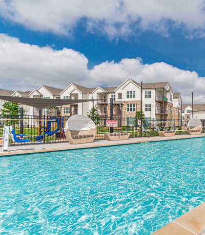 A swimming pool surrounded by a flower bed and apartment buildings in the background.at Crossroad Commons, Manor Texas