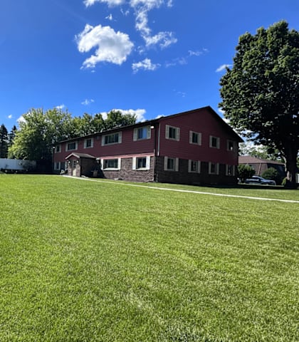 A large grassy field with a white building and a red building in the background.