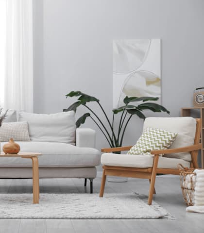 A living room with a white couch, a wooden chair, a wooden table, and a potted plant.