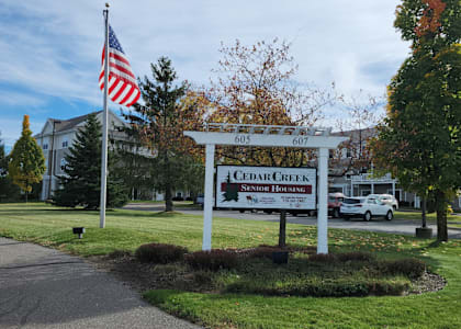 A sign for Cedar Creek Senior Housing stands in front of a building.
