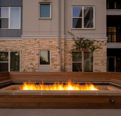 a large fire pit with a wooden bench around it in front of an apartment building