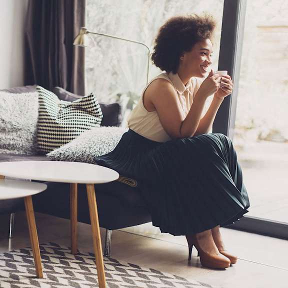 A woman sits on a couch with a white table in front of her.