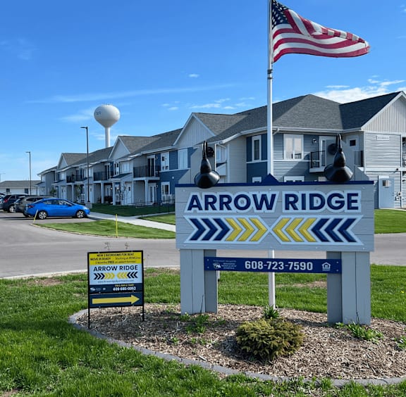 A sign for Arrow Ridge with a blue car parked in front.
