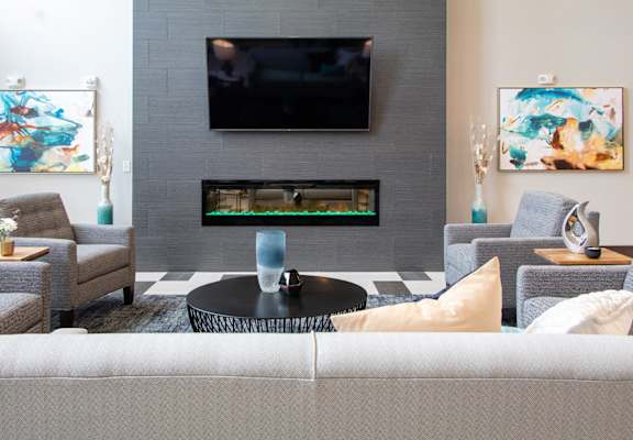 A living room with a grey couch, a black coffee table, a flat screen TV, and two paintings on the wall.