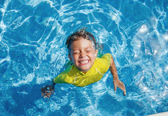 boy floating in bright blue swimming pool