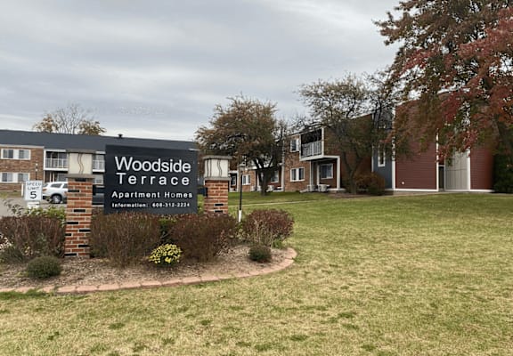 A sign for Woodside Terrace Apartment Homes is displayed in front of a grassy area.