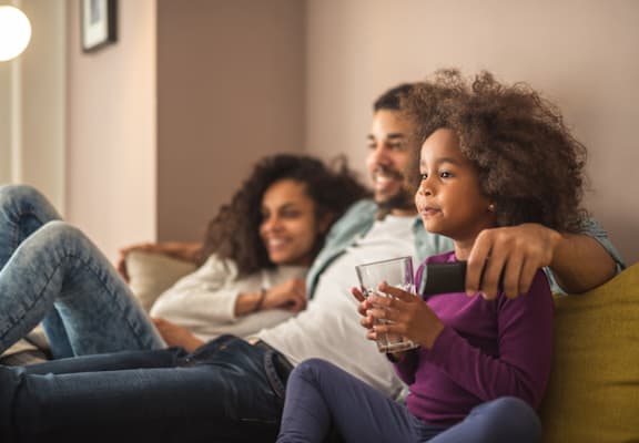 parents and young daughter sitting on couch watching tv at TOWNSHIP Apartments, CANBY