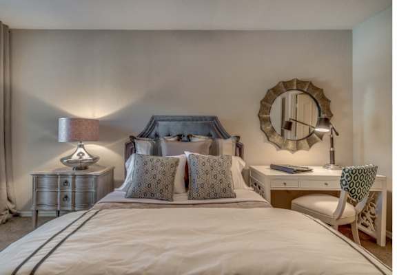 Furnished model bedroom with queen bed, nightstand, desk and chair.