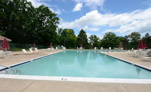 a swimming pool with chaise lounge chairs and trees in the background at Liberty Gardens Apartments, Baltimore